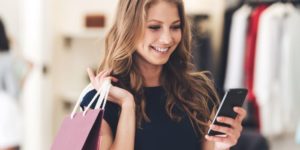 Making the retail connection. Beautiful young woman with shopping bags using her smart phone with smile while standing at the store