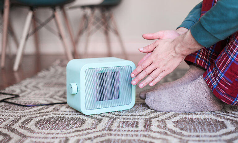 Hombre calentándose las manos con un calefactor eléctrico.