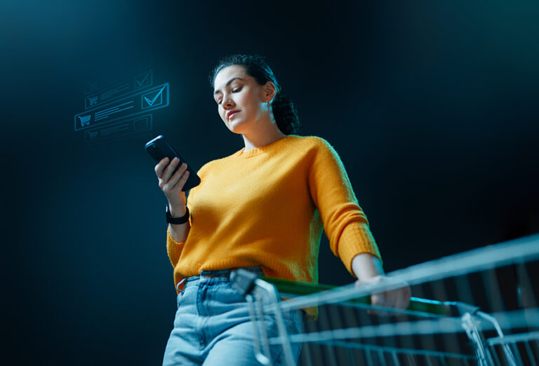 Mujer comprando online desde el smartphone con un carrito de la compra.
