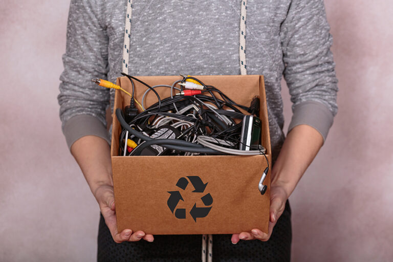 Mujer sosteniendo una caja llena de residuos electrónicos.