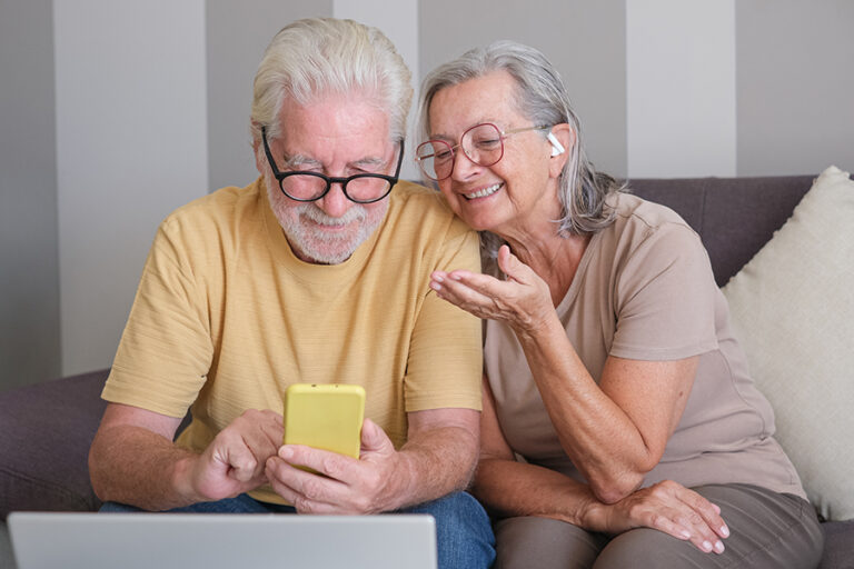 Pareja sénior usando el smartphone frente al portátil.